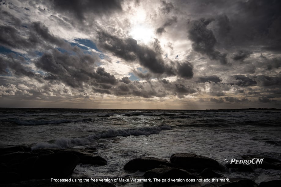 a photo of the ocean and sky with dark clouds and sun shining through