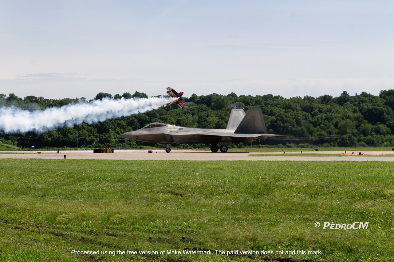 an F-22 sitting on a runway with Skip Stewart doing acrobatic procedures behind it