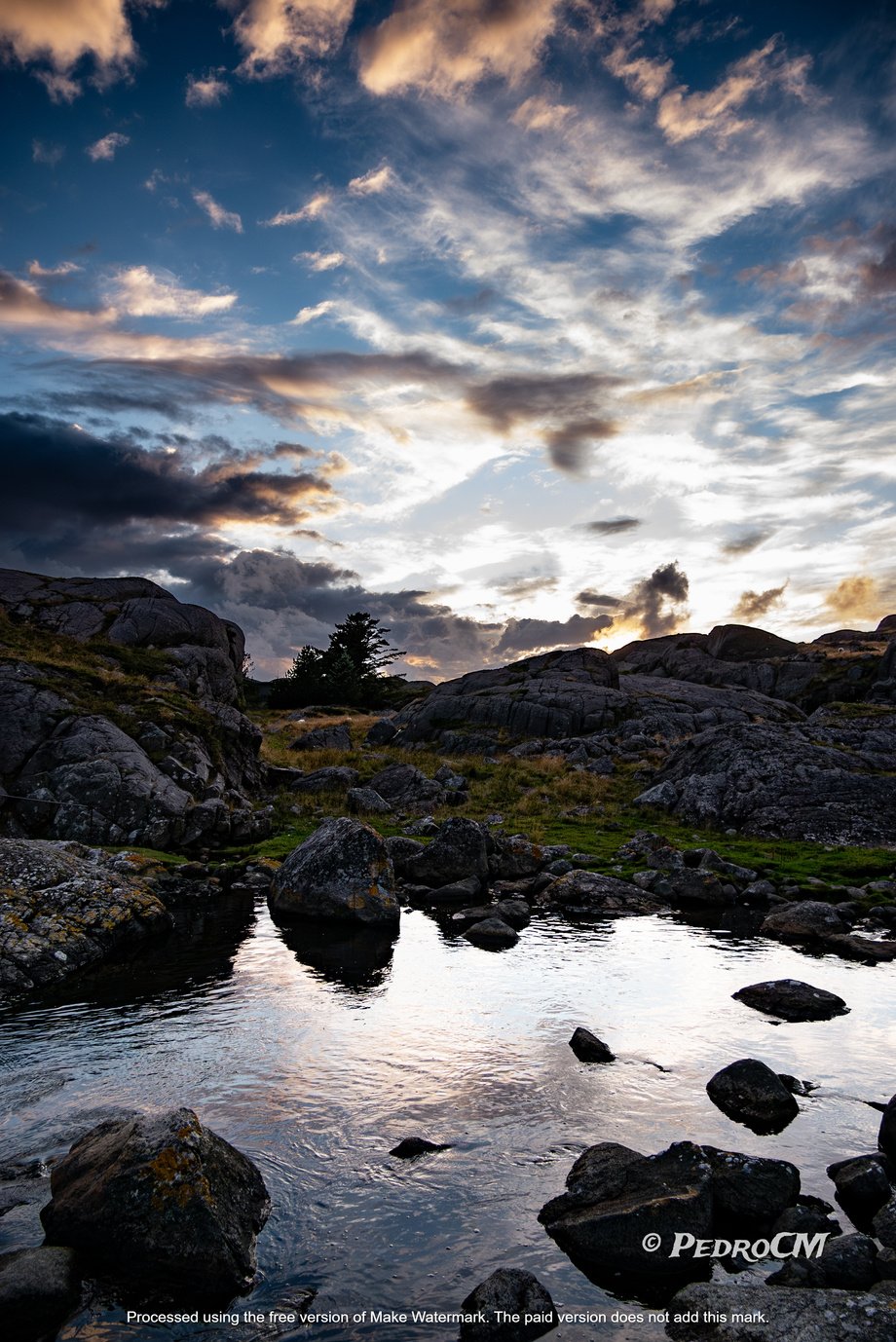 a picture of the edge of a rocky shore with rocks and clouds in the background with a scenic sky